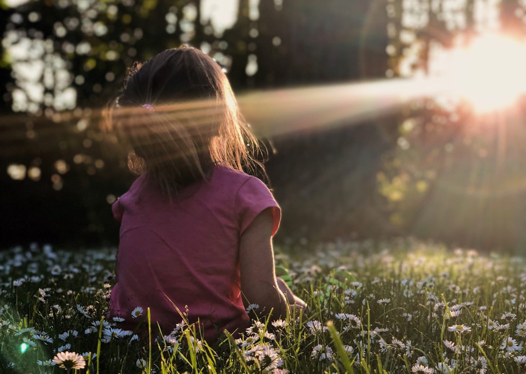 Little girl sitting in the forest with sun shining on her