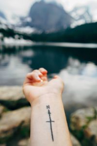 Woman with tattoo of arrow on wrist overlooking a lake