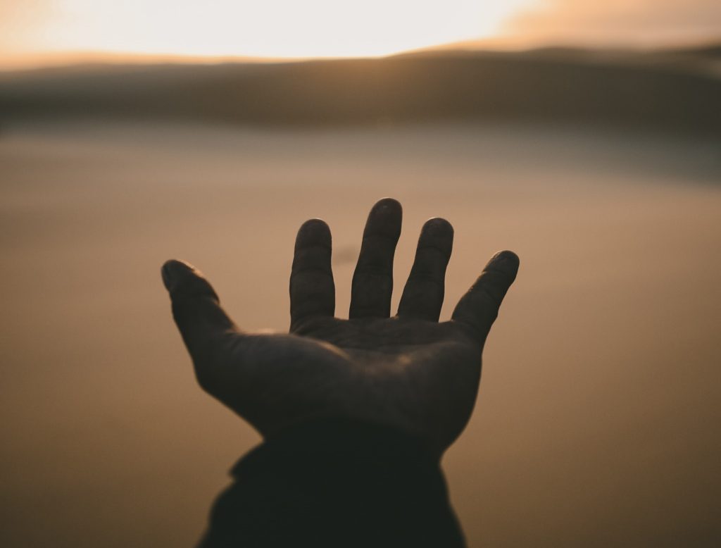 Open hand over body of water at sunset